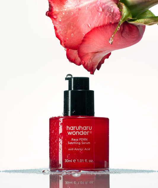 Red serum bottle with black cap labeled 'haruharu wonder' next to a pink rose on a white background